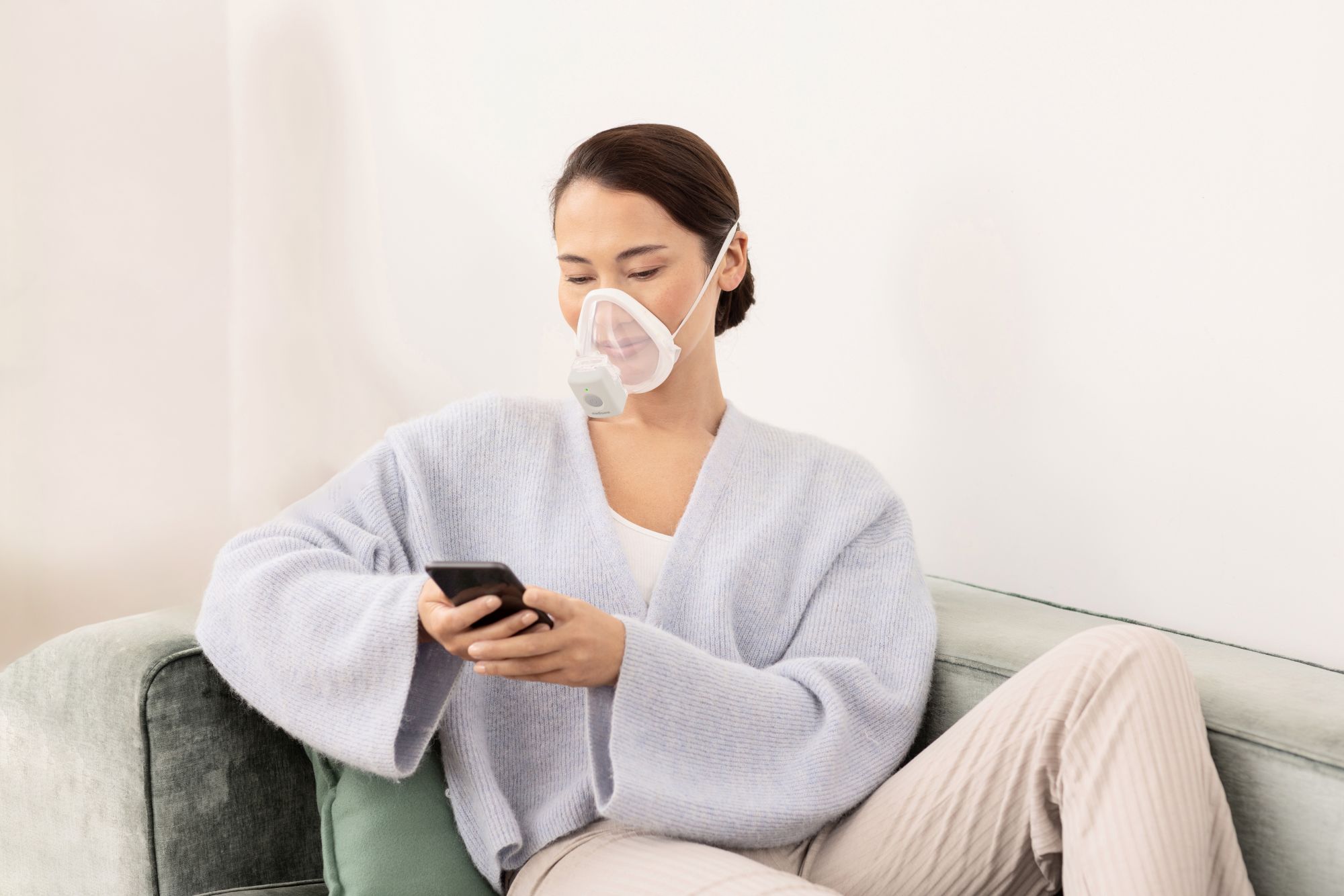 Woman uses the medisana IN 705 inhaler with mask comfortably on the sofa - effective inhalation therapy for respiratory diseases