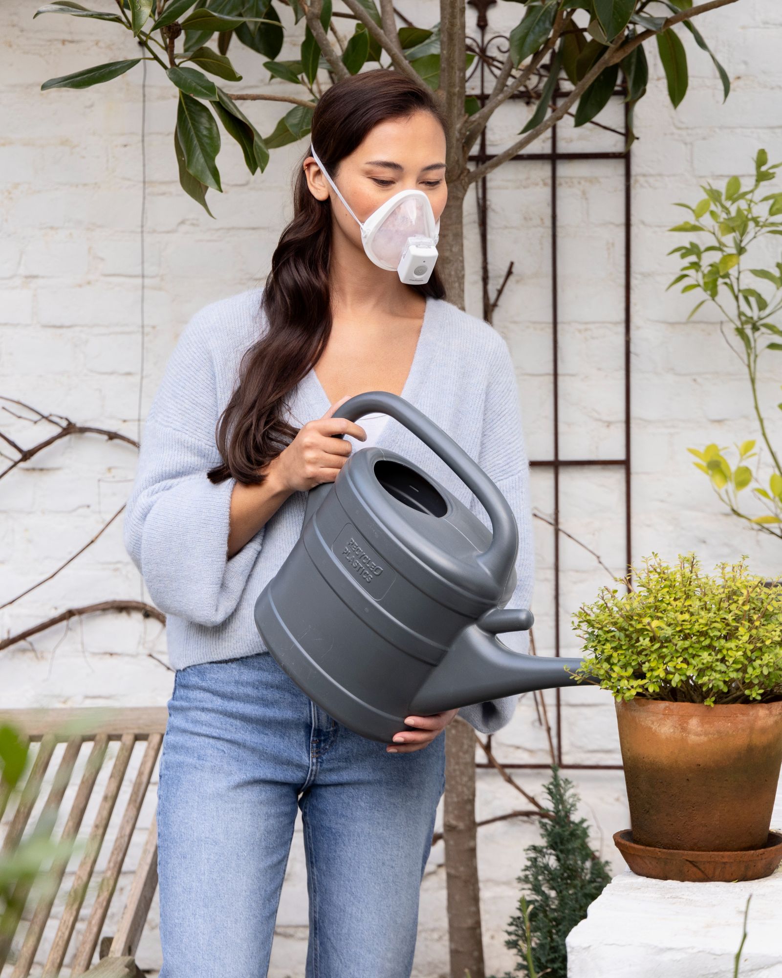 Woman wears medisana IN 700 inhaler with mask while watering plants - mobile inhalation therapy for more freedom in everyday life